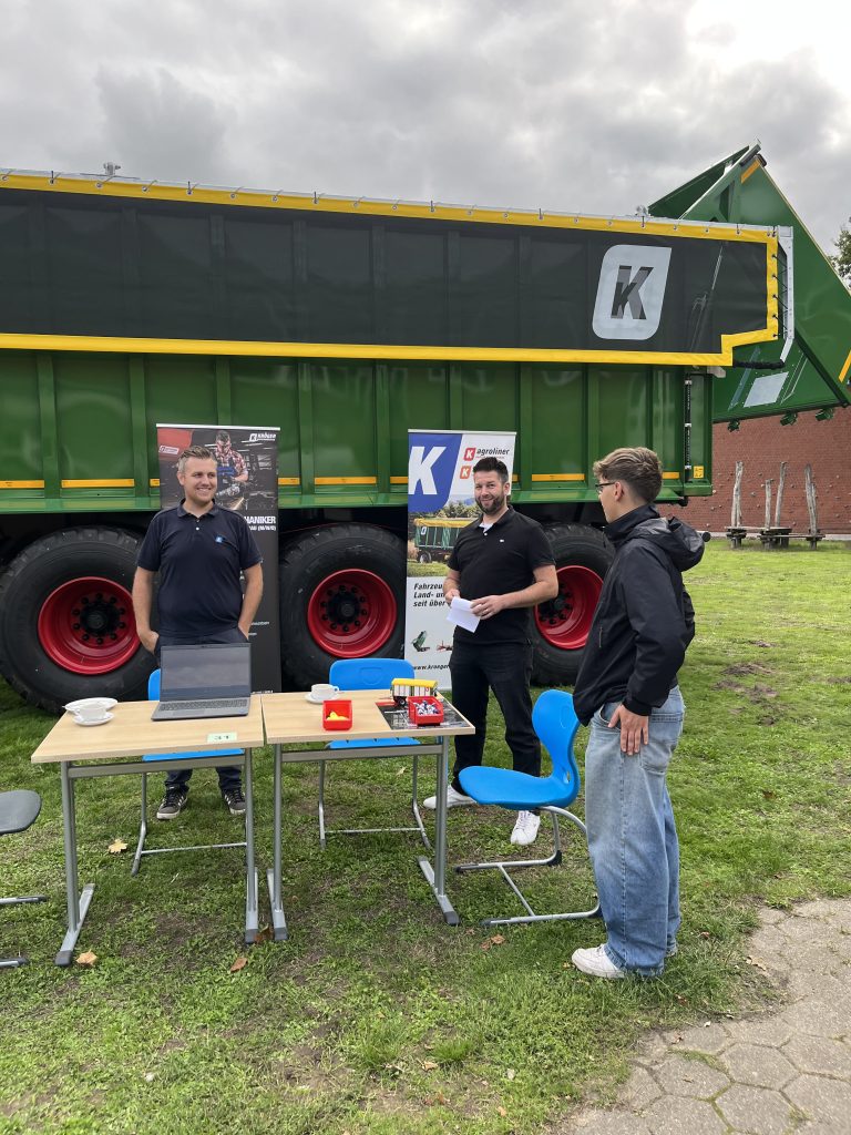 Gespräch an einem Messestand vor einem großen landwirtschaftlichen Anhänger.