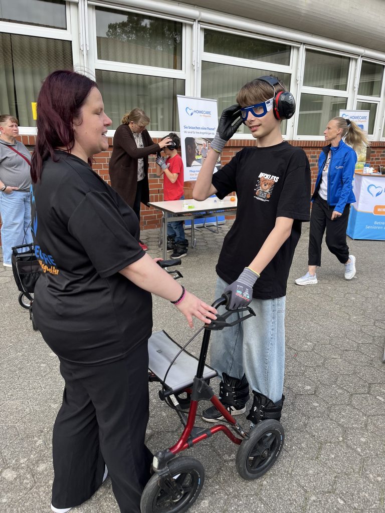 Jugendlicher mit Gehörschutz und Rollator an einem Informationsstand.