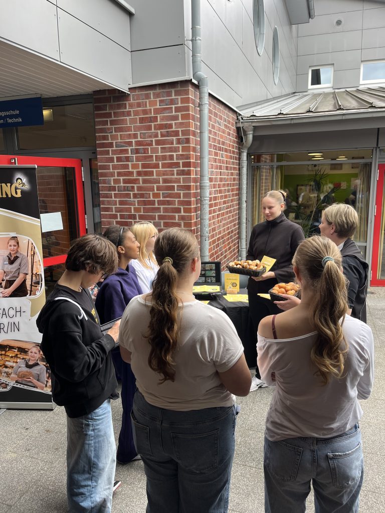 Jugendliche stehen an einem Informationsstand mit Gebäck.